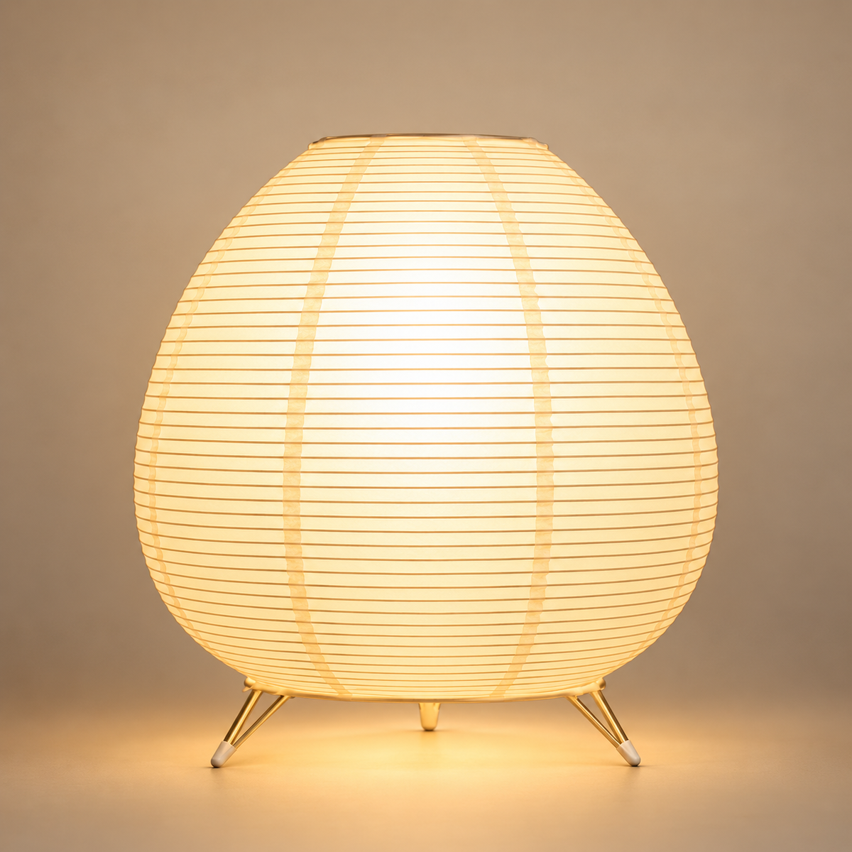 Lampe de Chevet Lanterne Ovale en Papier - Eclipsea | Cocon de Lune - allumée sur fond neutre, abat-jour ovale en papier à fines lattes et trois pieds dorés