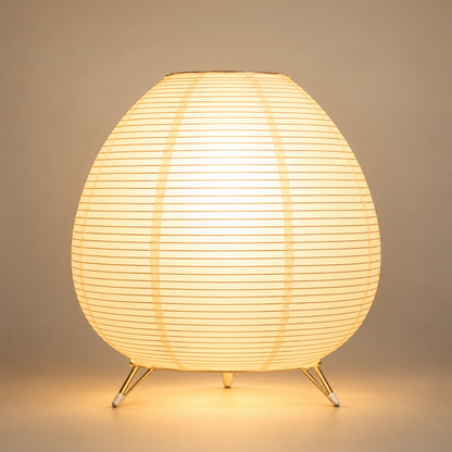 Lampe de Chevet Lanterne Ovale en Papier - Eclipsea | Cocon de Lune - allumée sur fond neutre, abat-jour ovale en papier à fines lattes et trois pieds dorés